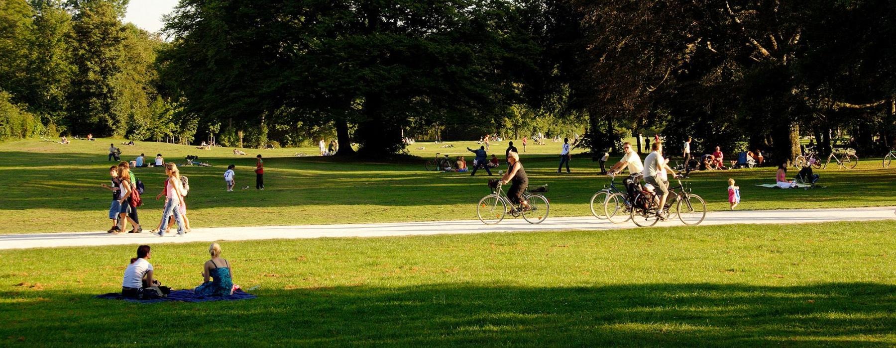 A park with many people riding bikes, having a picnic, and walking.
